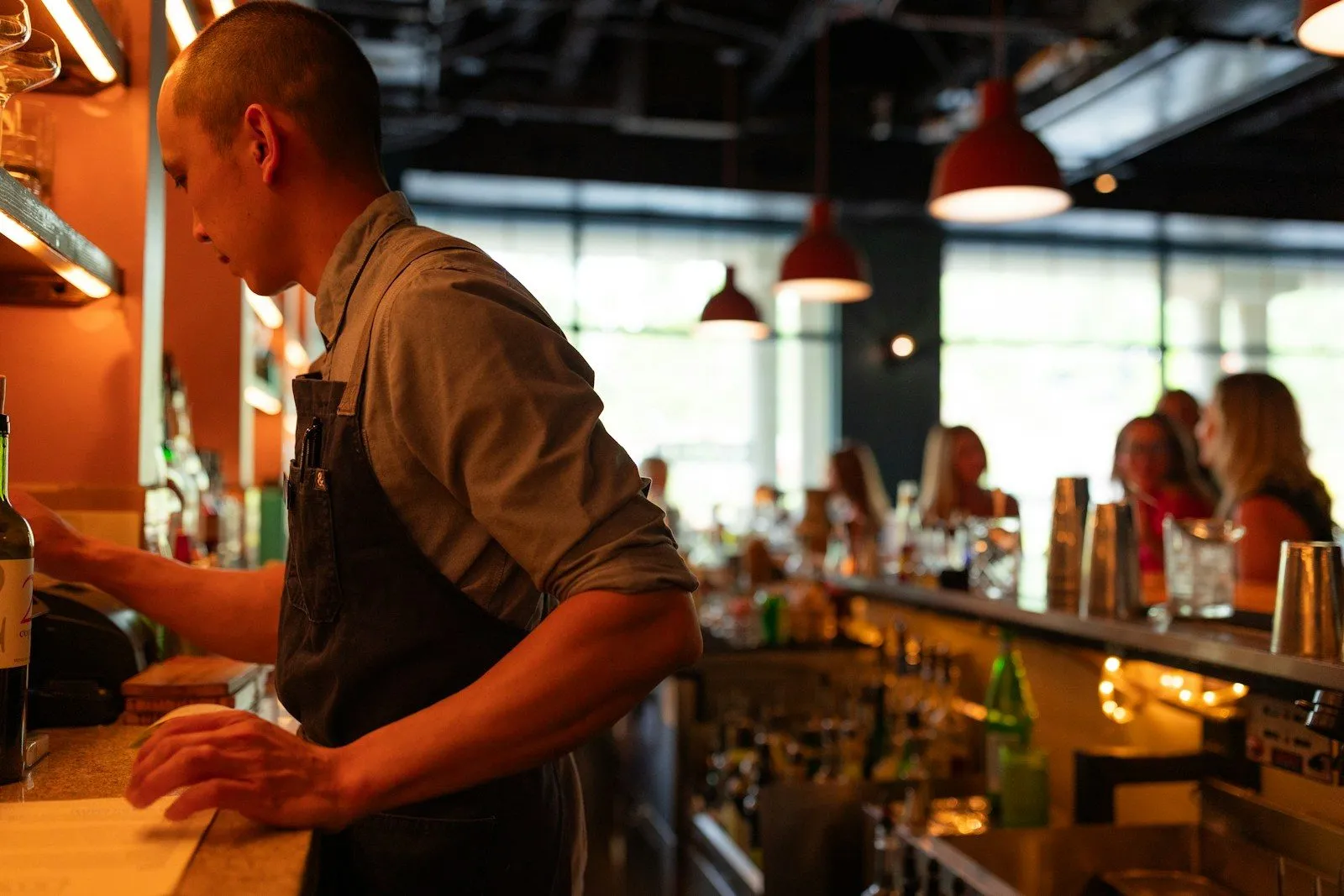 A man standing at a bar with a bottle of wine