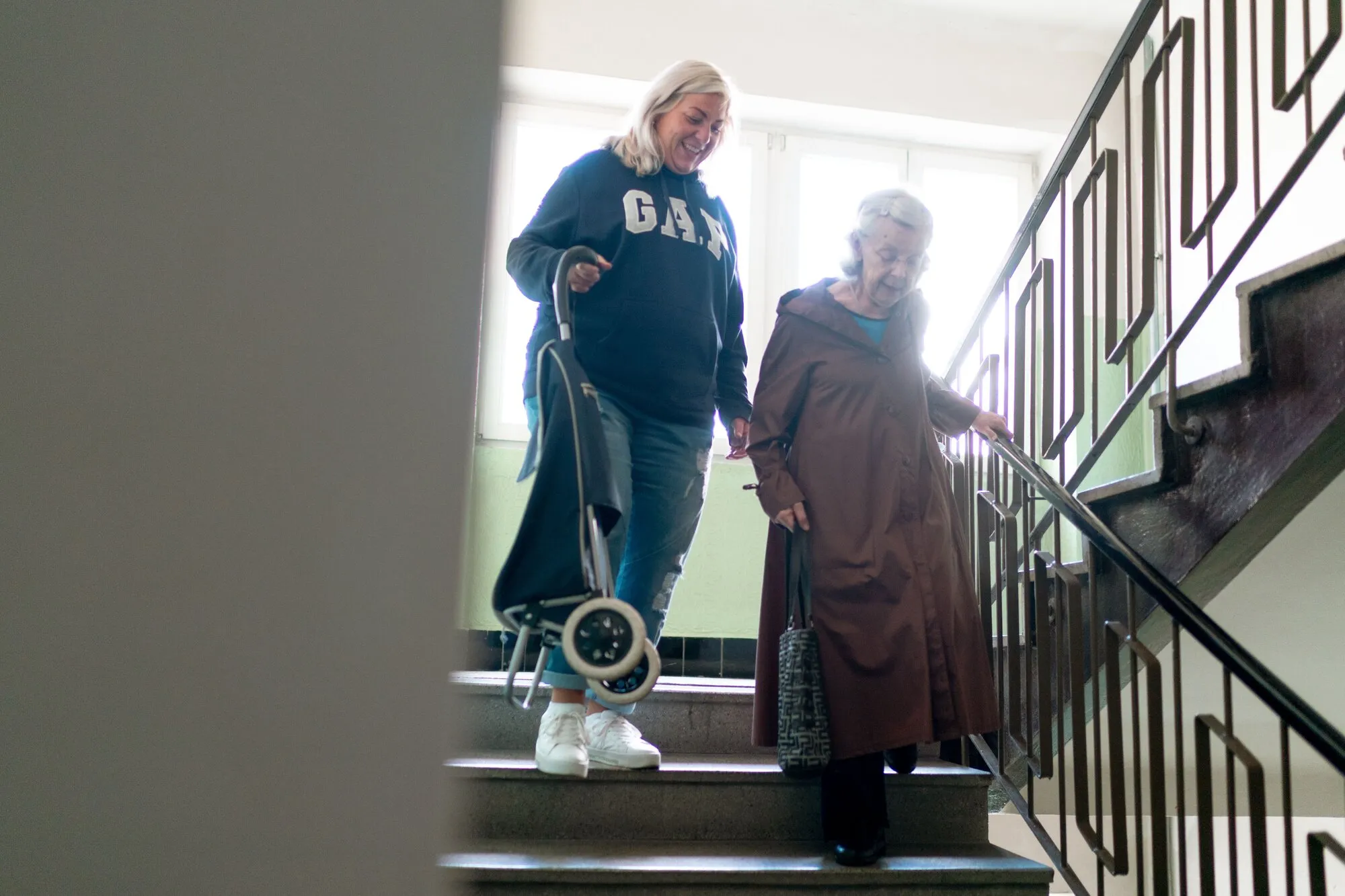 Home care worker smiling while helping a senior carefully down indoor stairs.